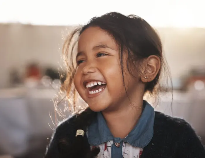 A photo of a little girl smiling in the sunshine.
